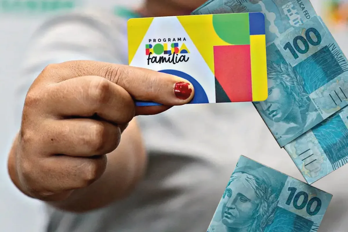 Cartão do programa Bolsa Família segurado por uma mão, junto com cédulas de dinheiro.