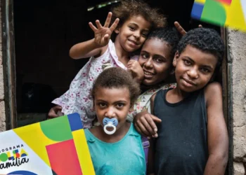 Crianças sorrindo em frente a uma casa simples, simbolizando beneficiários do Bolsa Família.