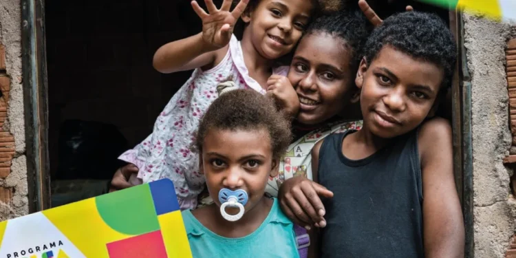 Crianças sorrindo em frente a uma casa simples, simbolizando beneficiários do Bolsa Família.