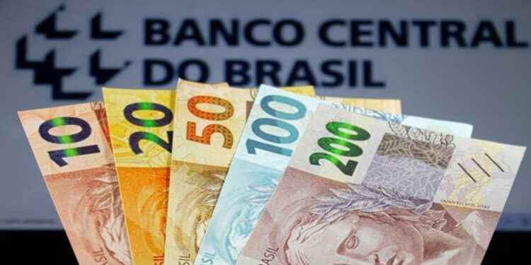 Notas de real em destaque frente ao logotipo do Banco Central do Brasil.