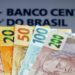 Notas de real em destaque frente ao logotipo do Banco Central do Brasil.