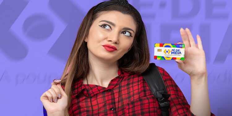 Mulher segurando um cartão colorido com a logo do programa 'Pé-de-Meia' enquanto olha para o lado, usando uma camisa xadrez vermelha e com um fundo roxo desfocado.