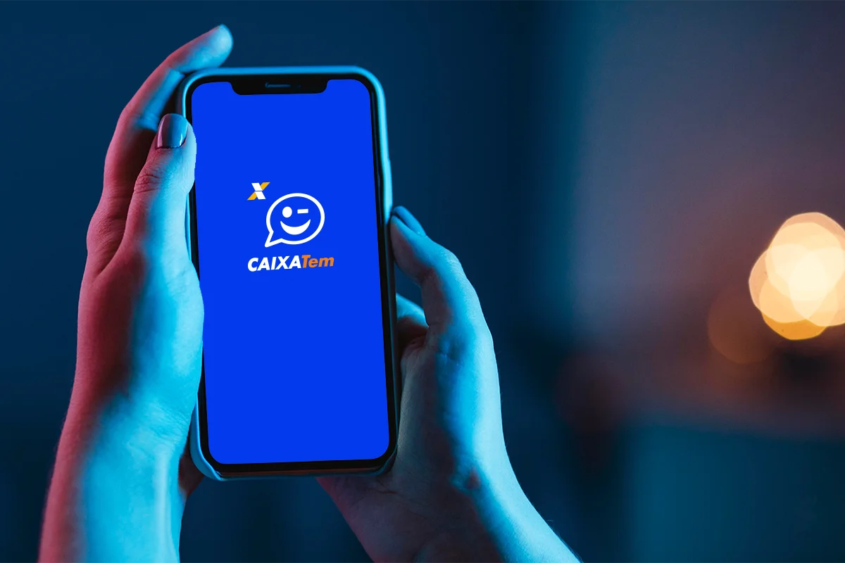  Pessoa segurando celular com o aplicativo Caixa Tem aberto em fundo desfocado