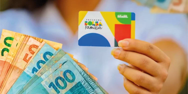 Pessoa segurando cartão do Bolsa Família e leque de cédulas em mãos
