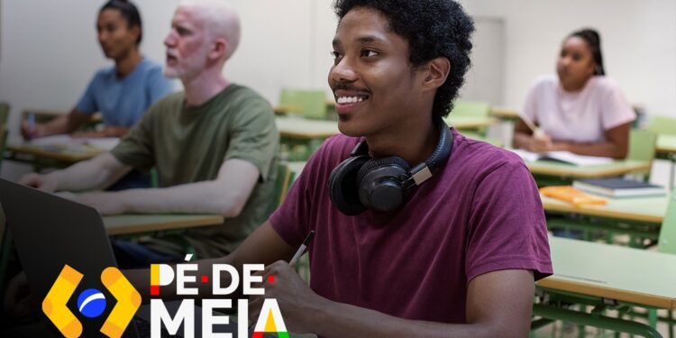 Estudante sorrindo enquanto usa um laptop em uma sala de aula, com outros colegas ao fundo. O logo do programa 'Pé-de-Meia' aparece na parte inferior da imagem.