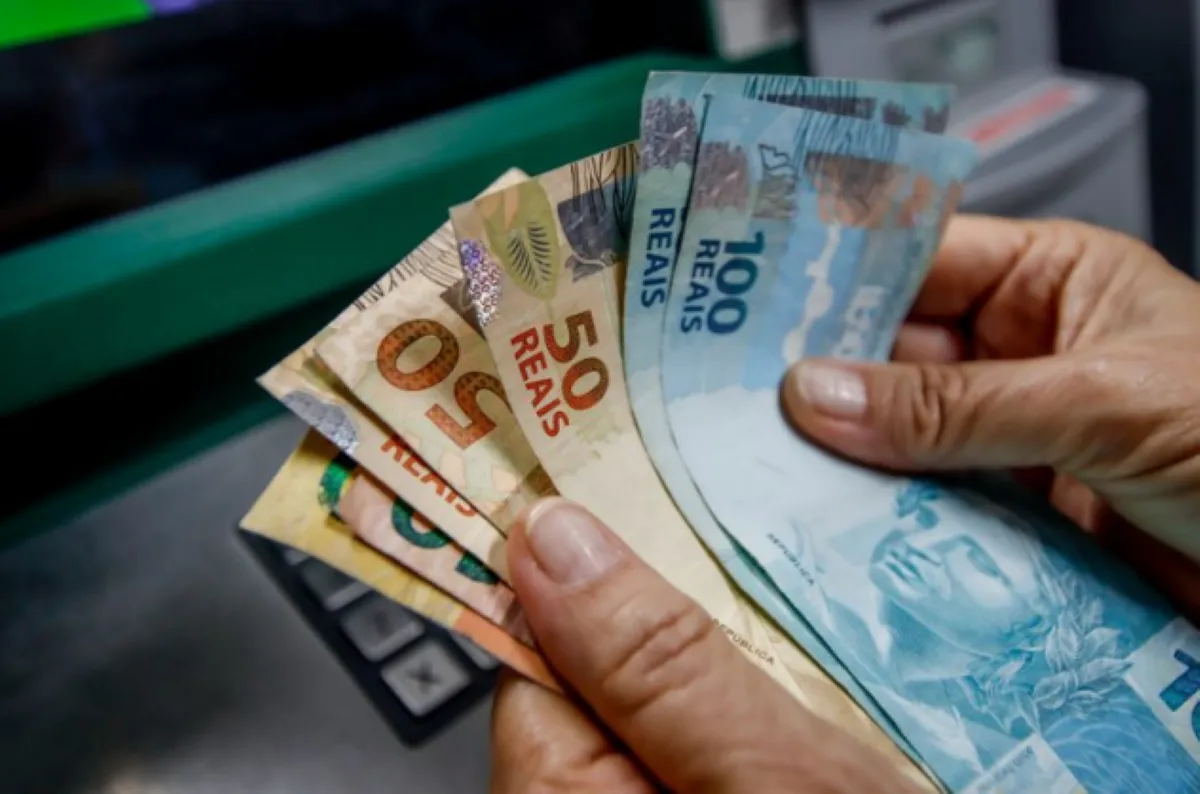 Mão segurando cédulas de reais, ilustrando o saque emergencial do FGTS.