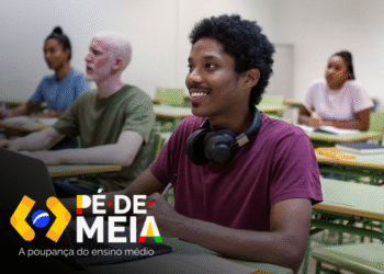Estudantes em sala de aula com foco em jovem sorrindo. Logo do programa Pé-de-Meia 2025 visível, representando a poupança do ensino médio.