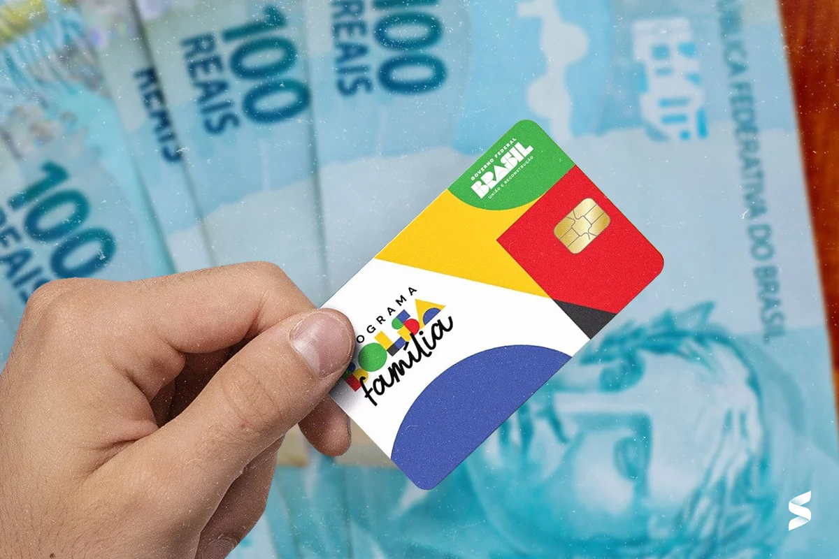 Pessoa segurando o cartão do Programa Bolsa Família com cédulas de 100 reais ao fundo.