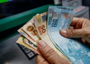 Cédulas de dinheiro brasileiro em mãos com foco nas notas de 50 e 100 reais.