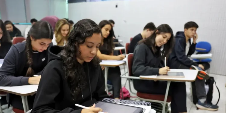 Estudantes participando de um curso gratuito, utilizando tablets e cadernos, com foco em aprendizado digital.