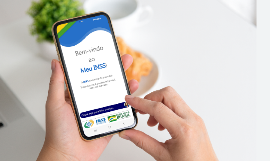 Mão segurando smartphone com aplicativo do INSS aberto, exibindo interface de login para acesso a serviços de aposentados e pensionistas.