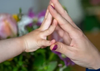 Mão de criança tocando a mão de um adulto com esmalte roxo, em gesto de conexão