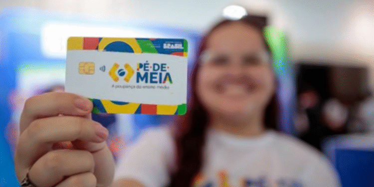 Mão segurando um cartão do programa Pé de Meia do governo brasileiro, com foco em apoio financeiro para estudantes em 2025