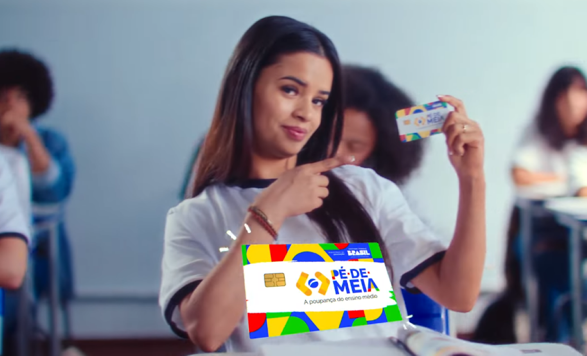 ovem segurando um cartão Pé de Meia em sala de aula com colegas ao fundo.