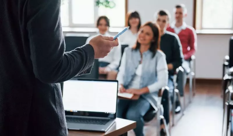 Professor explicando para grupo de estudantes em sala de aula.