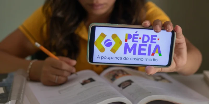 Estudante exibindo o aplicativo Pé de Meia em seu celular enquanto estuda, representando o calendário de pagamentos do programa para 2025.