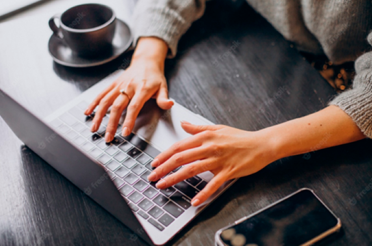 Pessoa digitando no laptop com uma xícara de café ao lado, com tema sobre cursos gratuitos do programa CadÚnico.