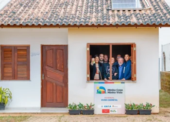 Grupo de pessoas sorrindo na janela de uma nova casa do programa Minha Casa, Minha Vida, mostrando a chave da moradia. Moradias pelo governo.