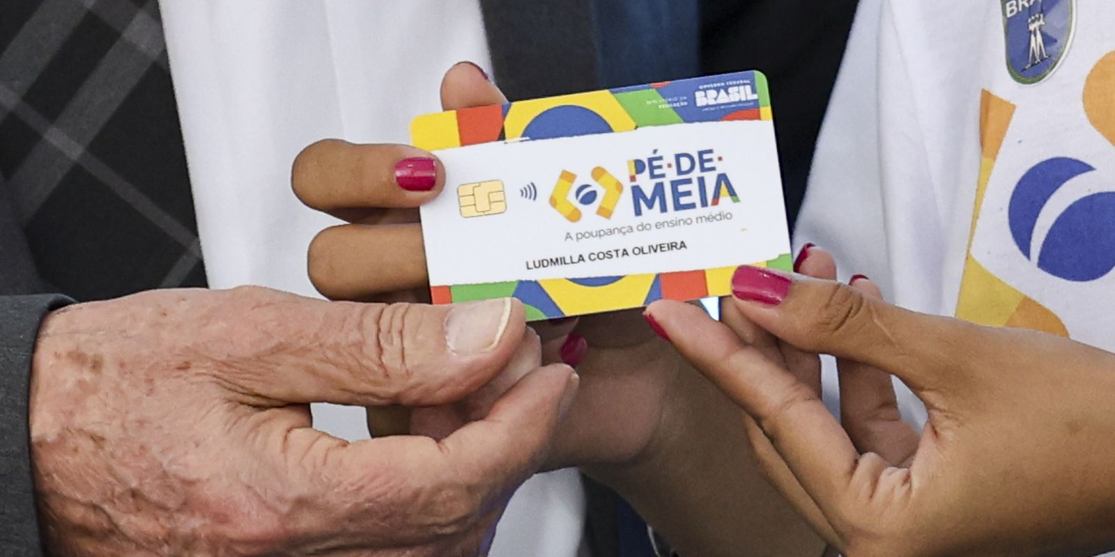 Cartão de crédito do programa Pé-de-Meia sendo entregue a uma estudante.