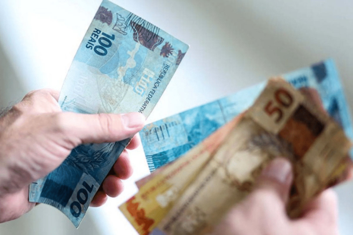 ENEM 2025! Como ganhar R$ 200 extras da participação no exame 2 Mão segurando notas de real brasileiro de 100 e 50, ilustrando ganhos financeiros.