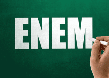 Mão segurando giz escrevendo a palavra ENEM em um quadro verde.